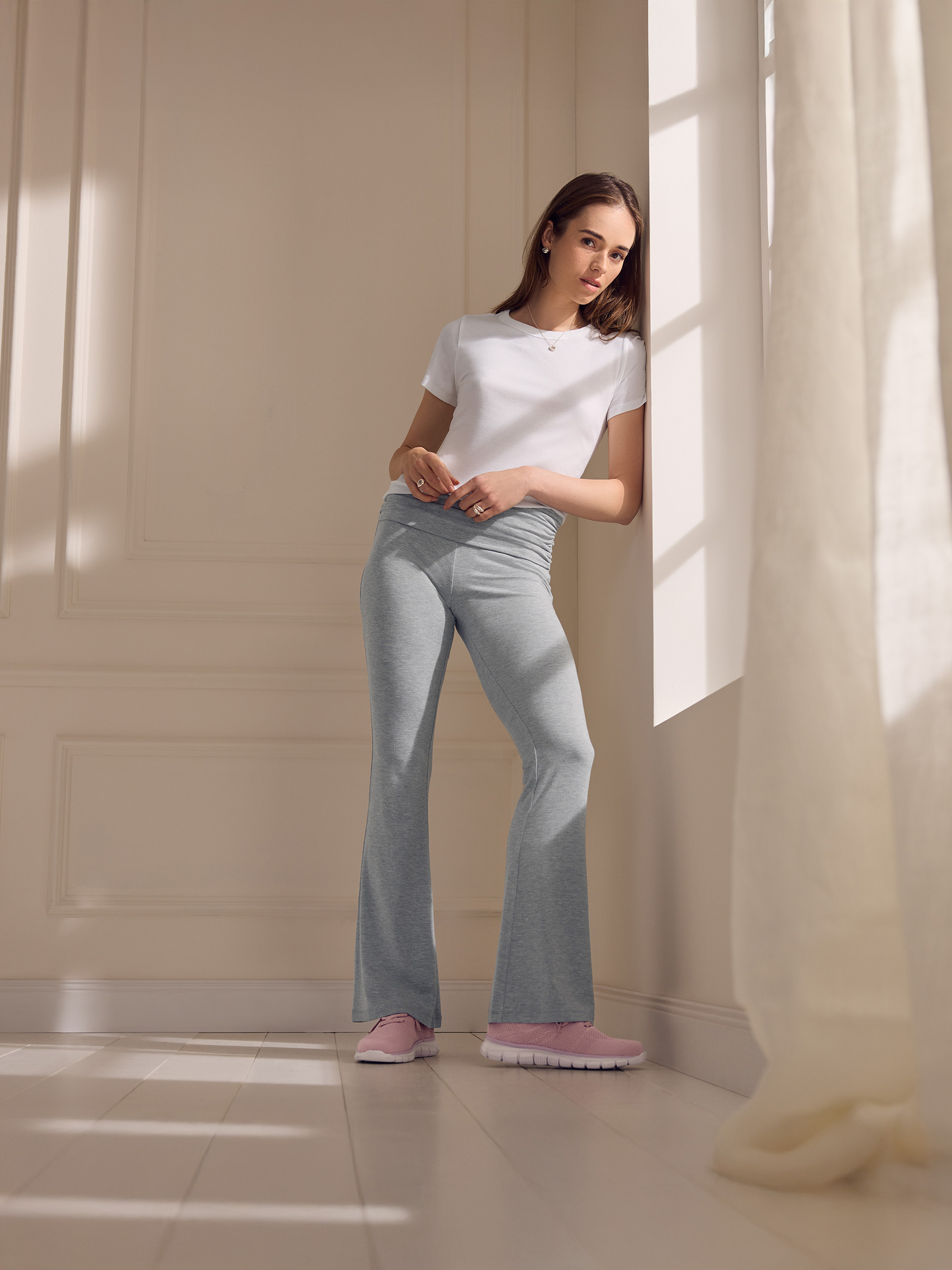 Vrouw in wit T-shirt en grijze joggingbroek leunend tegen een muur