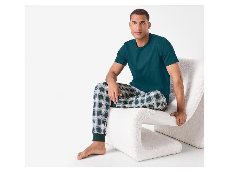 Man in groen geruite pyjama, zittend op een witte stoel.
