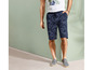Man draagt blauwe shorts met tropische print en grijze sneakers.