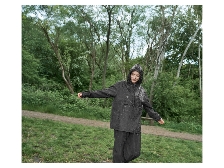 Vrouw in een donkere regenjas en -broek geniet van de regen in een park.