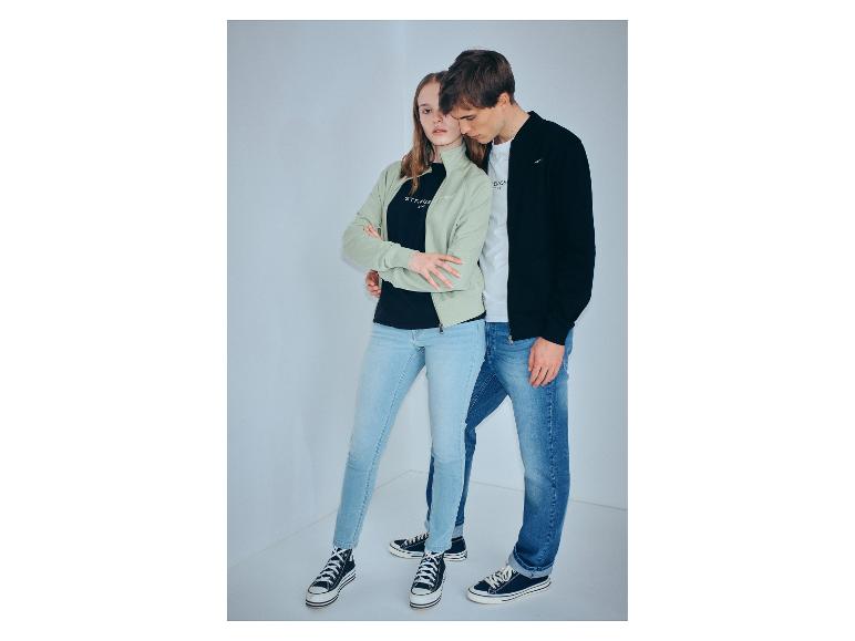 Koppel in jeans en sportieve jassen, met sneakers, in een witte hoek.