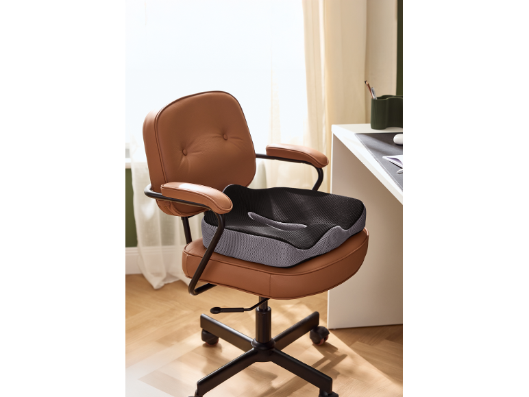 Ergonomisch kussen op een bruine leren bureaustoel in een thuiskantoor.