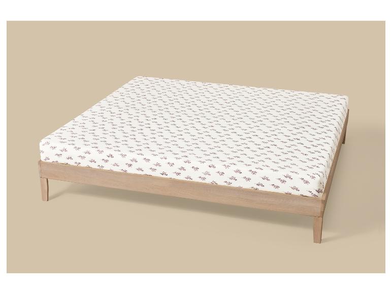 Bedframe met matras en wit hoeslaken met roodbruin bladpatroon.