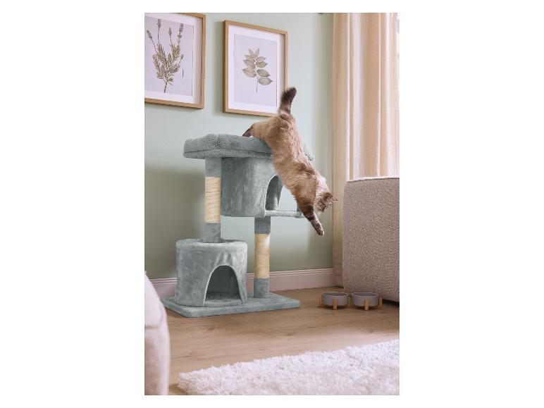 Kat springt van een meerlaagse krabpaal in een woonkamer met voerbakken.