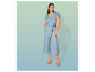 Een vrouw draagt een blauwe spijkerbroek jumpsuit met een riem en sandalen.