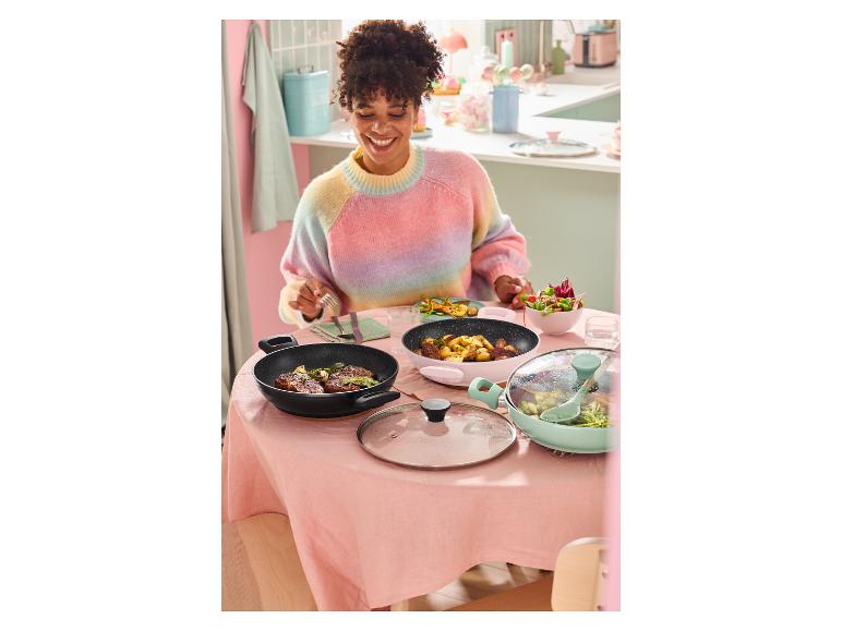 Een lachende vrouw aan tafel met kleurrijke pannen en eten.