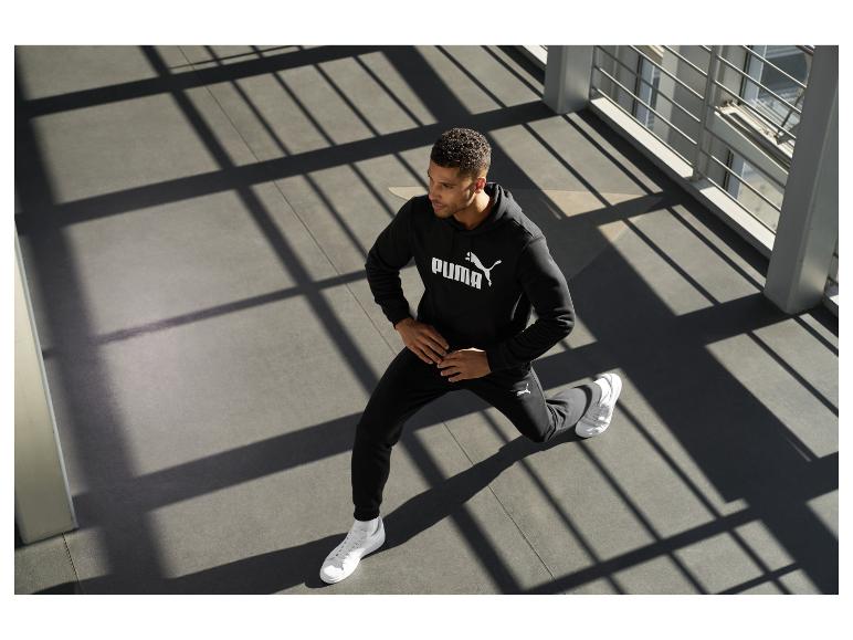 Man in zwarte hoodie en joggingbroek met wit logo, doet een lunge.