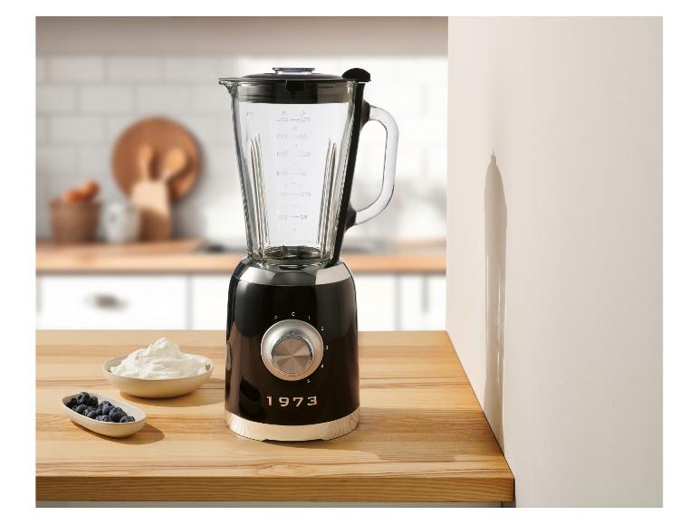 Een zwarte blender in 1973-stijl staat op een aanrecht in de keuken naast schaaltjes met yoghurt en bosbessen.