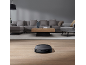 Robotstofzuiger op een houten vloer in een moderne woonkamer met een grijze bank.