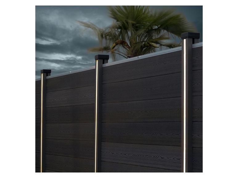 Donkere houten schutting met verticale LED-verlichting en een palmboom op de achtergrond.