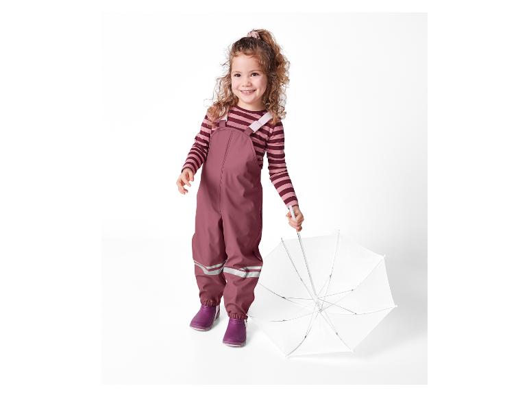 Een meisje in een roze broek en laarzen houdt een witte paraplu vast.