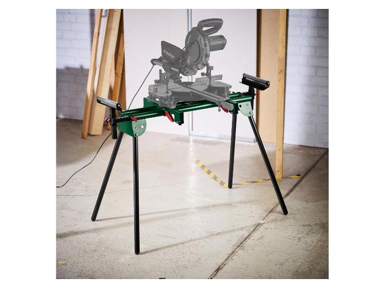 Groene afkortzaagstandaard met zwarte poten en grijze afkortzaag in werkplaatsachtergrond.