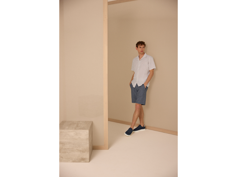 Man in een gestreept overhemd, blauwe short en sneakers.