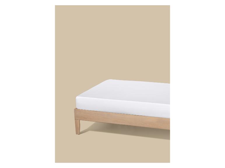 Wit matras op een houten bedframe tegen een beige achtergrond.