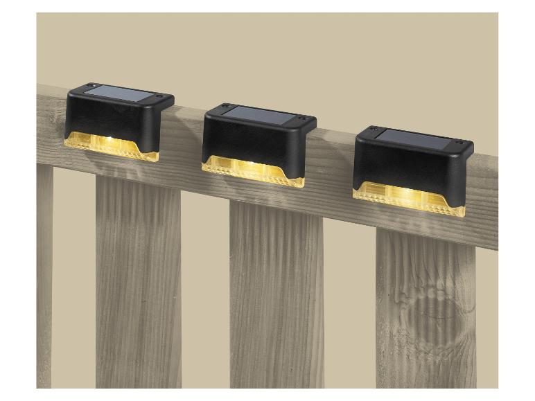 Drie zonnelampen voor terrassen die een houten hek verlichten.