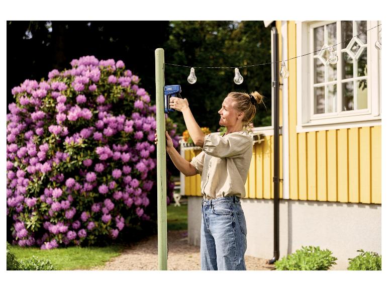 Vrouw gebruikt LIVARNO® Handtacker »RPC7« om lichtsnoer aan houten paal te bevestigen.