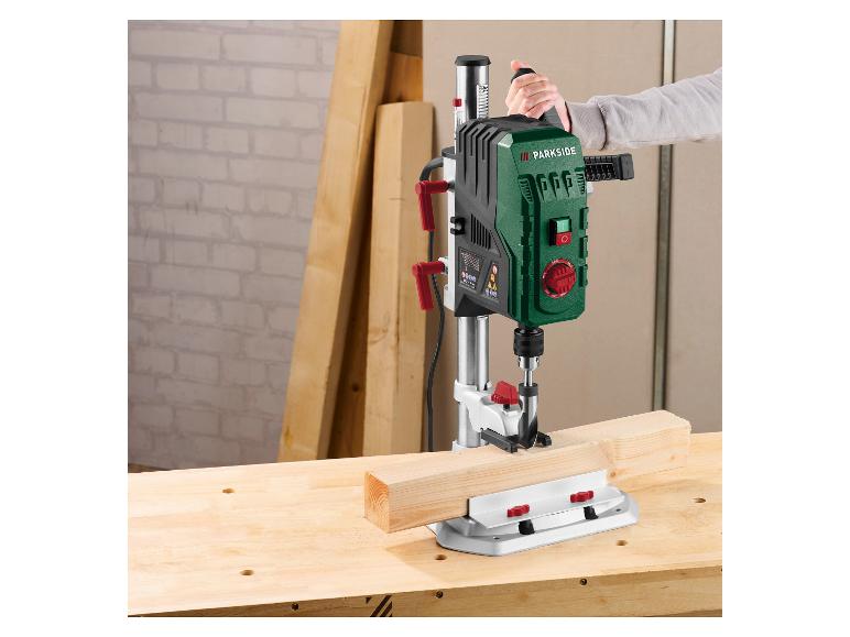 Persoon gebruikt een Parkside boorstandaard om in een houten balk op een werkbank te boren.