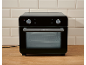 Zwarte mini-oven met glazen deur en bedieningspaneel op een houten aanrecht.