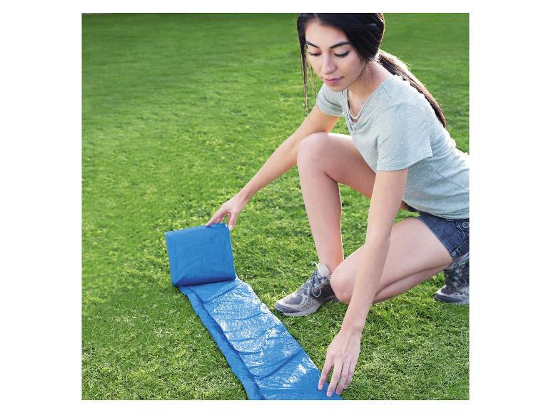 Een vrouw rolt een blauw zeil uit op het gras.