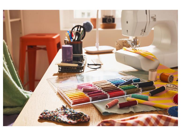 Een naaimachine en veel gekleurde draden op een houten tafel.