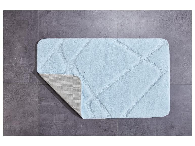 Een lichtblauw badmat met een ruitpatroon op een grijze tegelvloer.