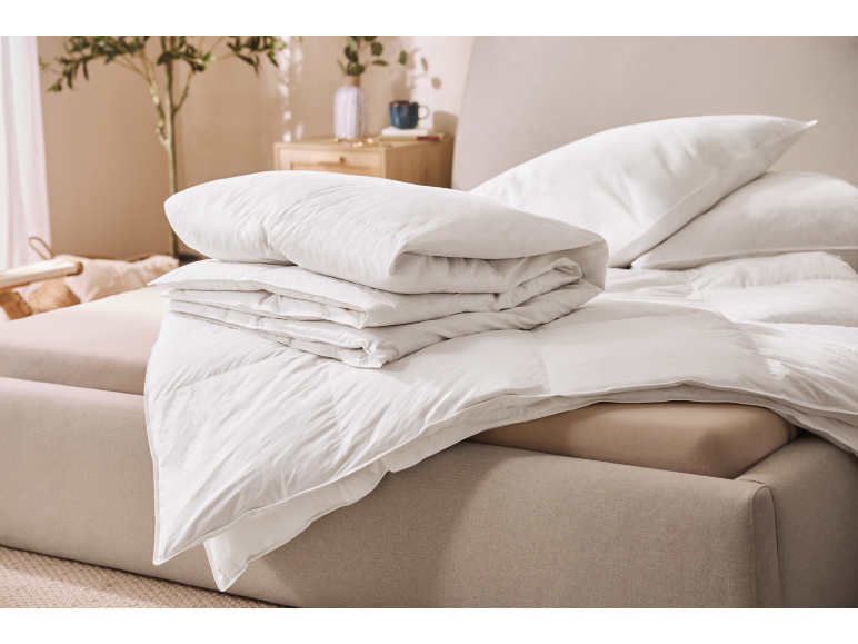 Witte donzen dekbedden en kussens op een bed in een lichte slaapkamer.