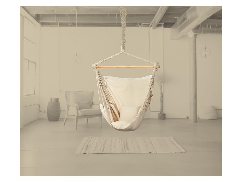 Hangende hangstoel in licht interieur met vloerkleed en fauteuil.