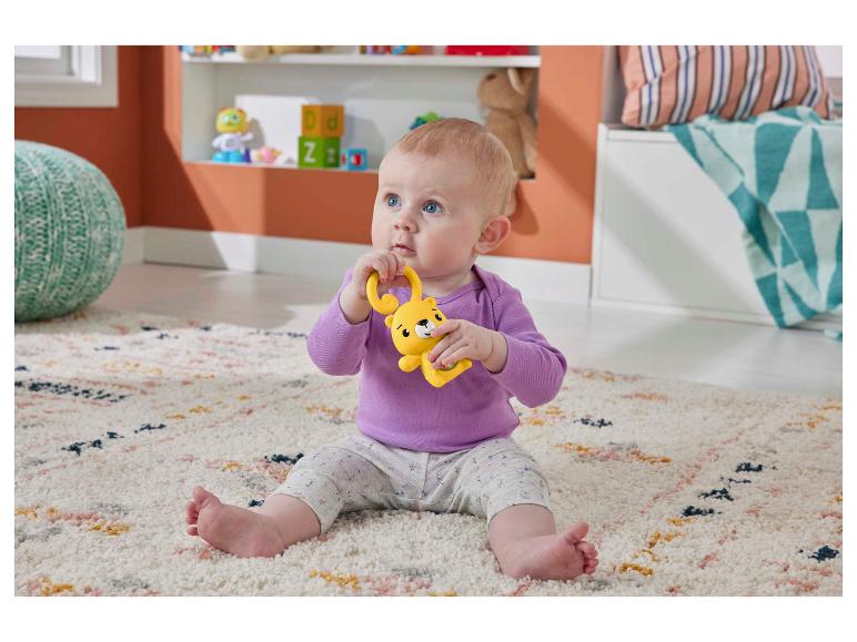 Baby zit op een vloerkleed met een gele apenrammelaar.