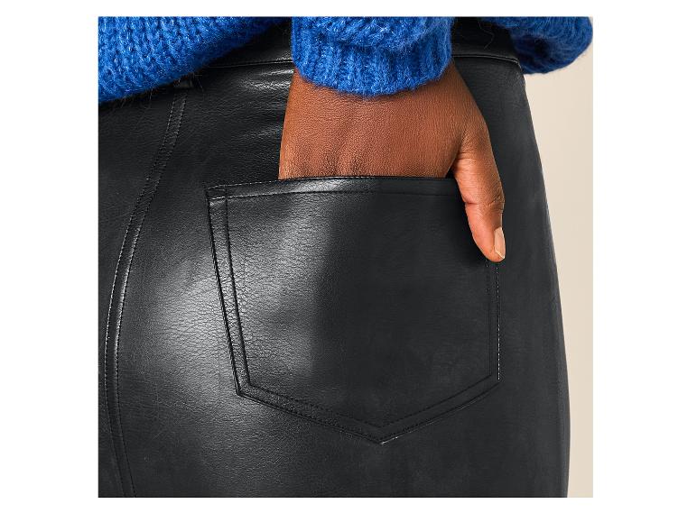 Donkere vrouw in blauwe trui en zwarte imitatie leren rok, met hand in zak.