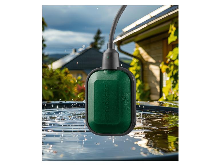 Groene vlotterschakelaar voor water in een ton, met regen en huis op de achtergrond.