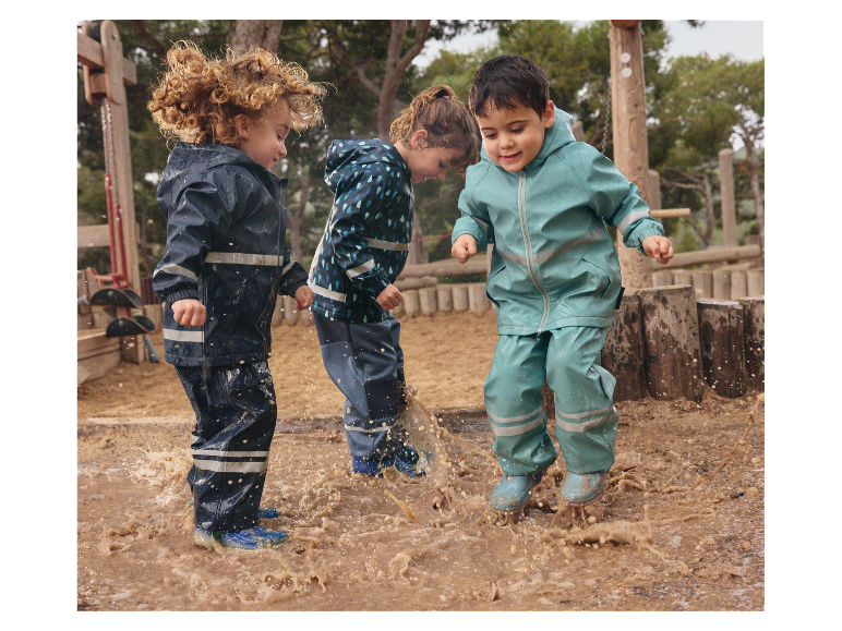 Drie kinderen spelen in een plas met hun regenkleding.