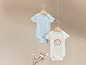 Twee babypakjes met korte mouwen, een lichtblauwe en een witte met regenboogprint.