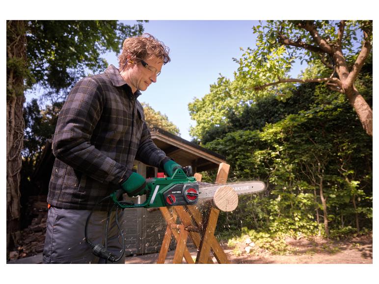 Man met veiligheidsbril en handschoenen zaagt hout met een kettingzaag buiten.