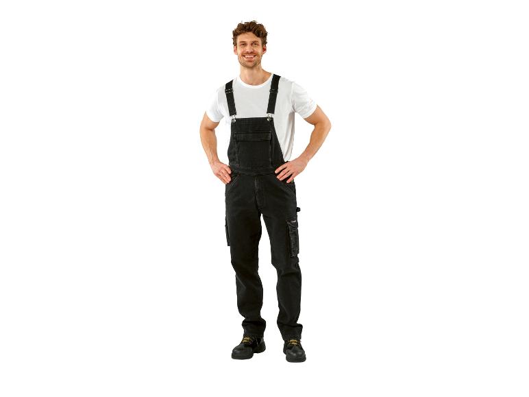 Lachende man in zwarte tuinbroek en wit T-shirt, handen in de zij.