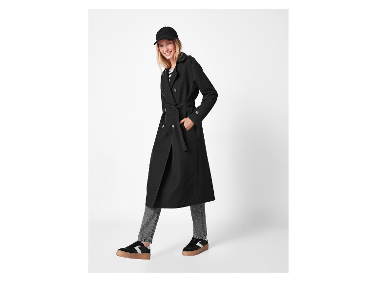 Model in een lange zwarte jas en sneakers.