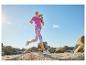 Vrouw rent in fuchsia T-shirt en bedrukte legging in rotsachtig landschap onder blauwe lucht.