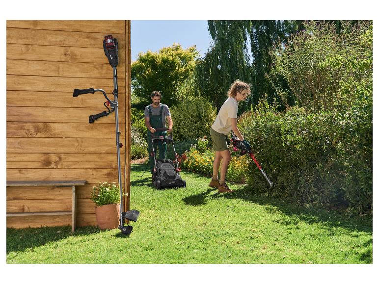 Man maait het gazon met een grasmaaier en vrouw snoeit de heg met een heggenschaar in de tuin.