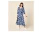 Vrouw in een blauw-wit patroon maxi-jurk met 3/4 mouwen en witte sneakers.