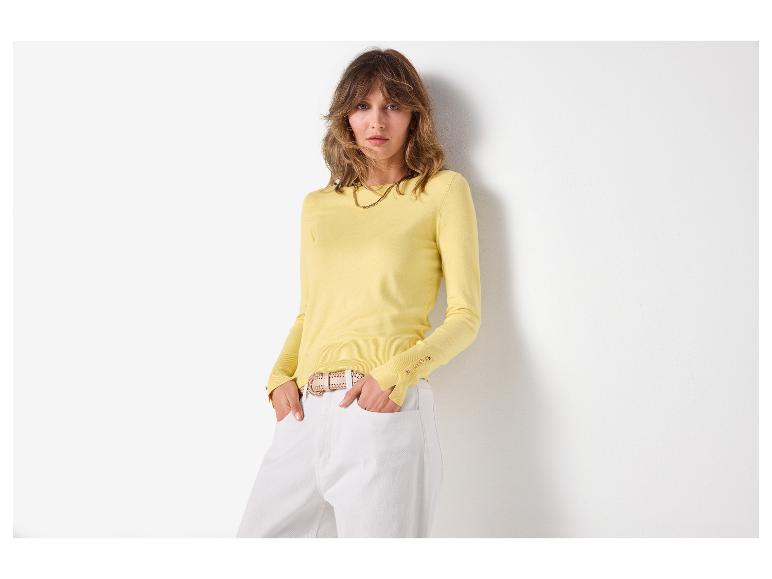 Vrouw in gele trui met lange mouwen en witte broek met riem