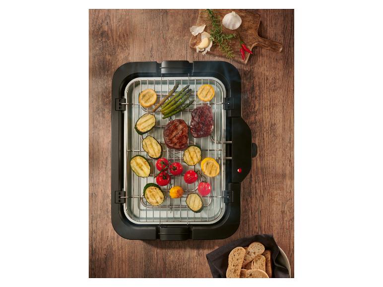 Elektrische grill met gegrild vlees en groenten, kruiden en brood op een houten tafel.
