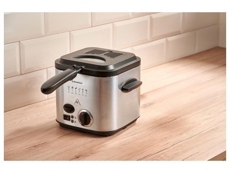 Compacte zilverkleurige friteuse met een zwart deksel, bedieningselementen en handgrepen, op een houten aanrecht.