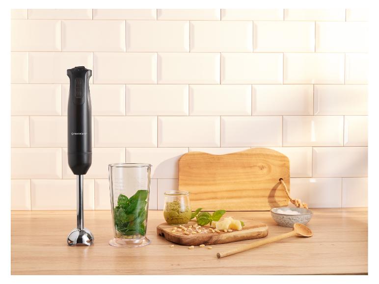 Staafmixer met pesto-ingrediënten op een houten aanrecht.