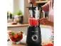 Vrouw maakt aardbeiensmoothie in zwarte blender, omringd door verse aardbeien.