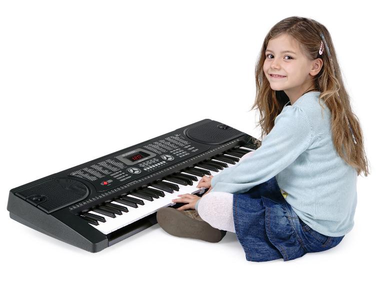 Een jong meisje zit op de grond en speelt op een zwart elektronisch keyboard.