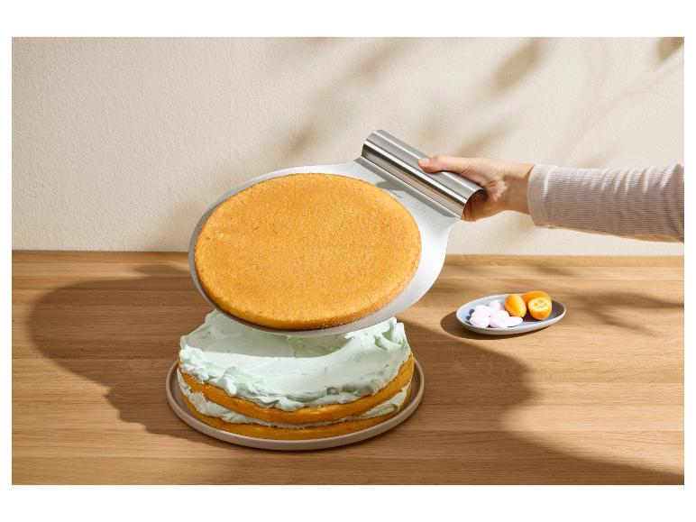 Hand plaatst ronde cakebodem met muntvulling op taart met metalen spatel.