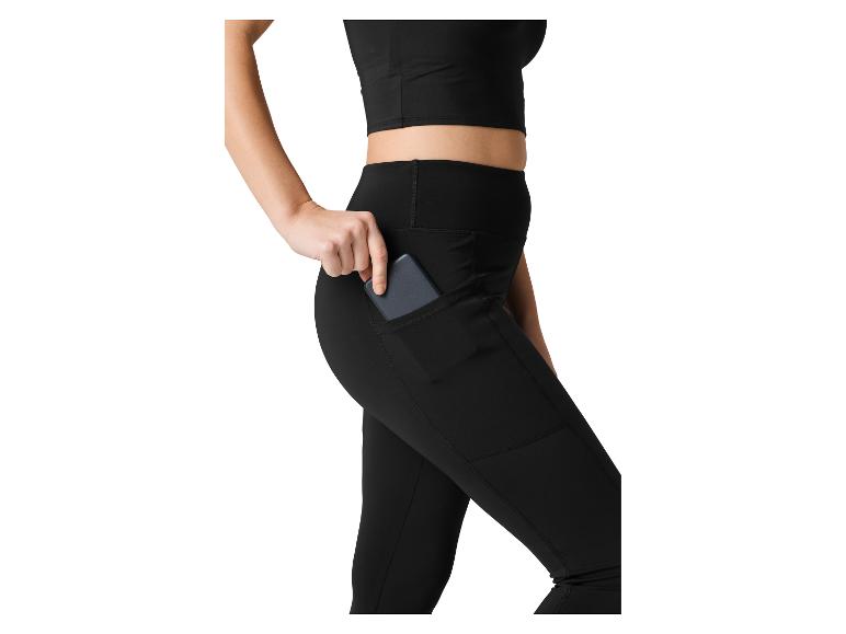 Vrouw in zwarte crop top en legging, stopt telefoon in zijzak.