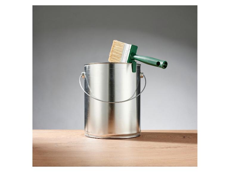 Groene verfkwast rustend op een metalen verfblik op een houten tafel.