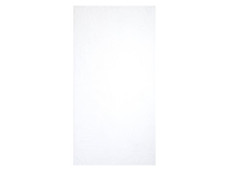 Een witte badhanddoek met een geborduurd patroon.