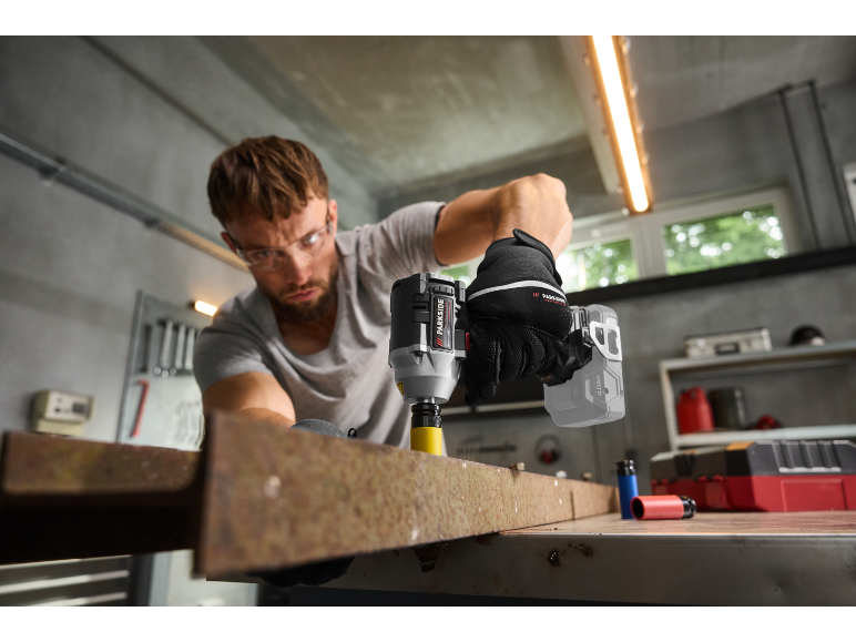 Man met veiligheidsbril gebruikt een slagschroevendraaier op een metalen balk.