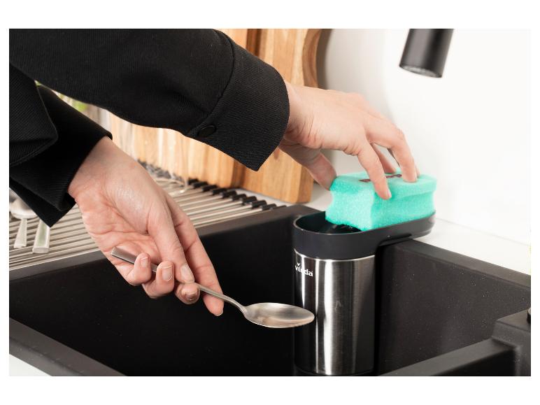 Handen wassen een lepel in een gootsteen met een spons en zeepdispenser.